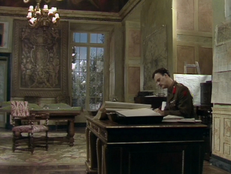 Darling in Melchett's office. Tapestry and window visible.