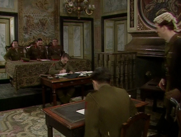 Reverse shot of the courtroom, with a different tapestry behind Melchett
