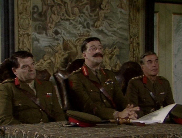 Melchett in the courtroom, with the new tapestry behind him