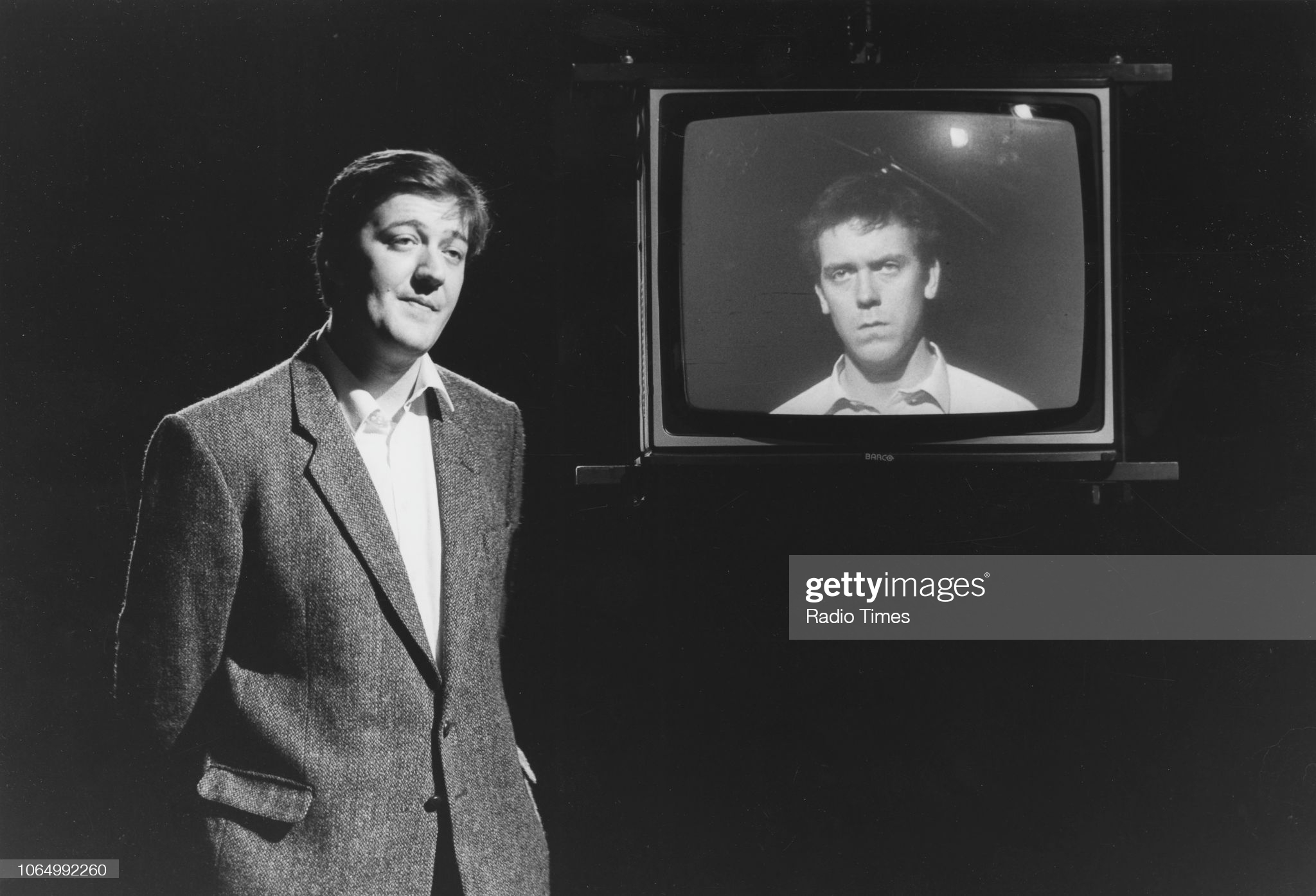 Comic actors Stephen Fry (left) and Hugh Laurie (on a television screen) on the set of a television show, December 17th 1988. (Photo by Don Smith/Radio Times/Getty Images)