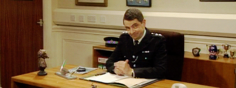 Inspector Fowler at his desk, greeting the audience