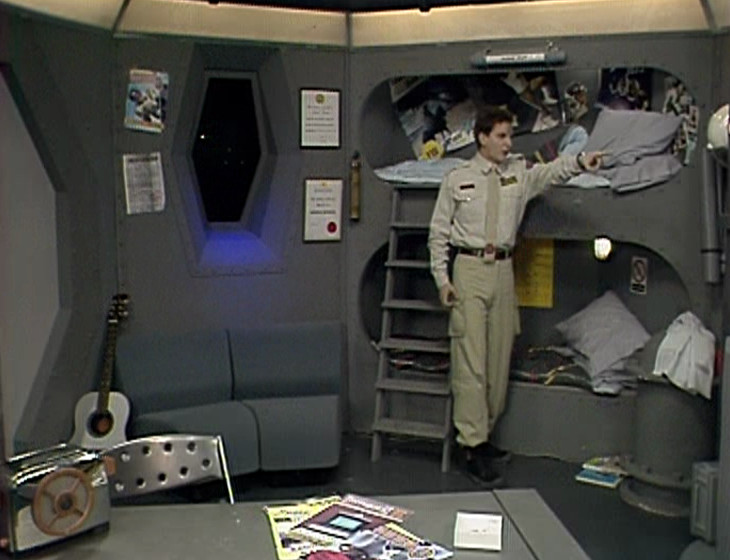 Rimmer pointing at Holly on the monitor
