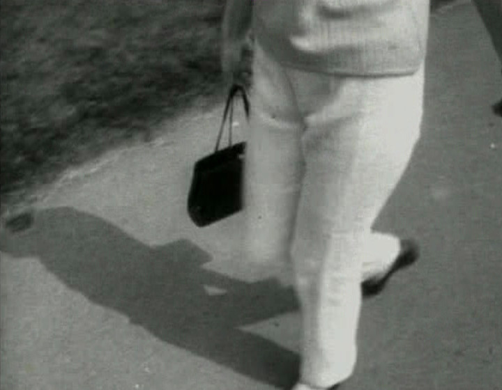 Woman walking down street carrying handbag and a radio