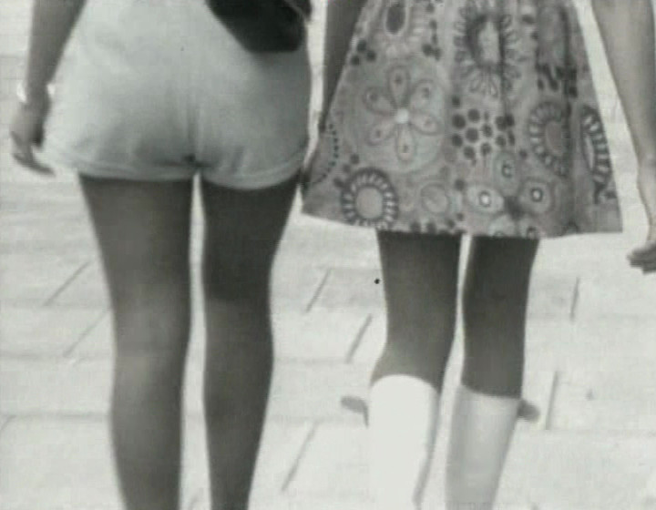 Black and white: two women walking down the street, the camera focusing on their bums