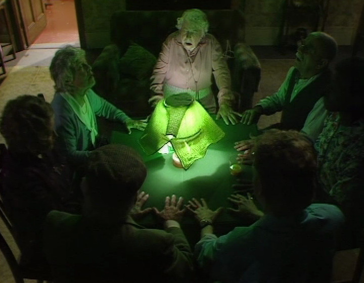 A seance from In Sickness and in Health, with everyone sitting round the table